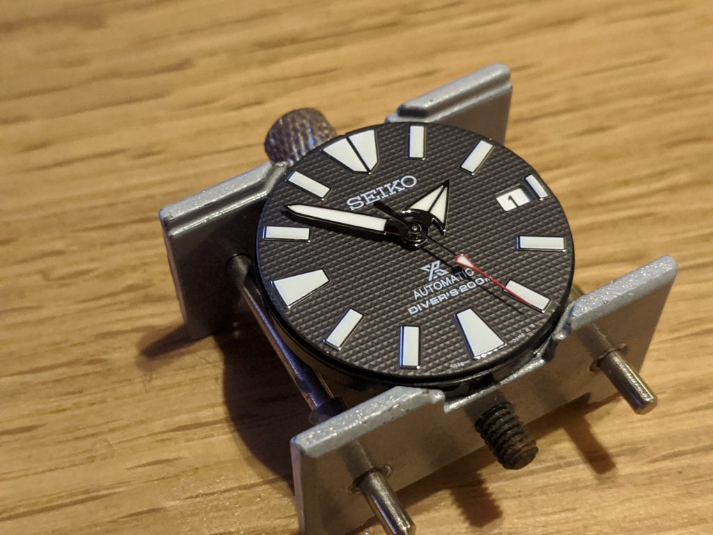 Seiko Samurai Waffle Dial, Movement & Hands displayed in a watchmakers movement holder. The watch hands have been repaired and reattached to the pinion of the Seiko 4R36 Movement . 