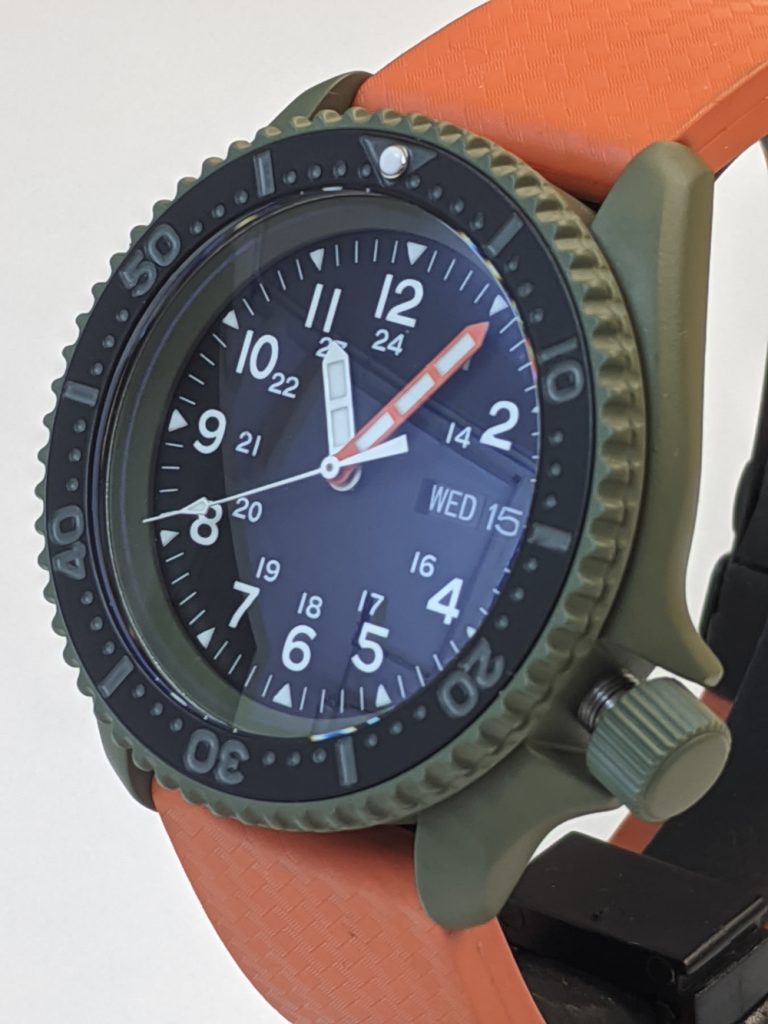 Seiko SKX - with a Green Cerakote coating case chapter ring, crown and bezel. Custom Cerakote bezel insert with hand painted numerals, Black Field style dial with an orange minute hand accompanying the white hour and second. Completed with a rubber strap with depoymentr clasp.