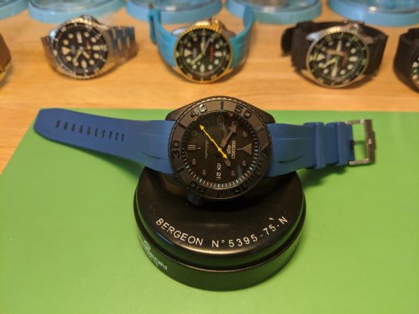 Seiko SRPD79 Blackout Mod - Blue Monstraps 2 peice. YM insert, chapter ring with blue hour markers, yellow lighting second hand, double dome sapphire with blue AR coating - displayed on a carbon seiko display stand infront More modified Seiko's