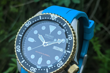 Seiko SKX 2 tone OEM Gold Plated bezel and crown completed with a light blue strap displayed infront of some shrubbery (bushes)