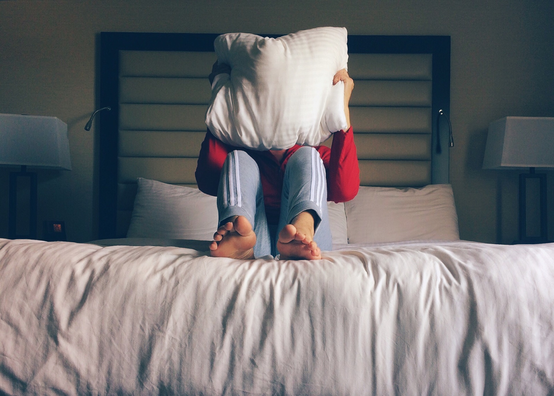 Ein Mann auf einem Bett hält sich ein Kissen vor sein Gesicht