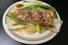 Bed of green leaved vegetables on spaghetti topped with cooked salmon with sprinkled sesame seeds on top