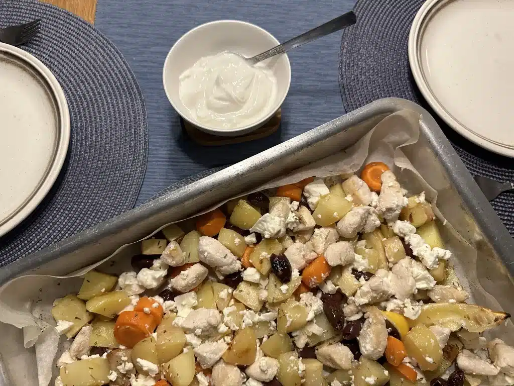 Baking tray with chicken slices, root vegetables and feta cheese with a side dish of Greek cheese