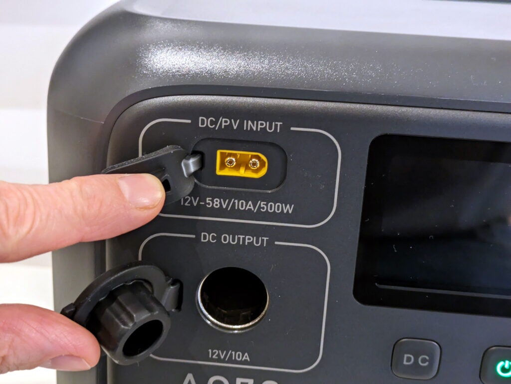 Detail of the DC input and output ports, their rubber bung covers held to the side by a finger and thumb