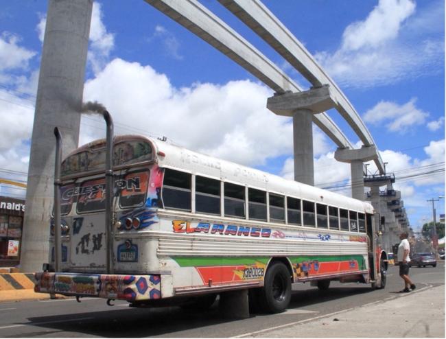 A metro line looms over a red devil. For bus painter Piri, a Panama City without diablos rojos buses is unimaginable. "That will be like a garden without roses. A sky without stars.”