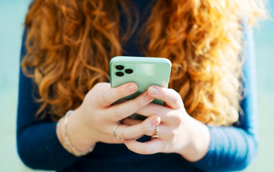 A red-headed woman holding a mobile phone. 