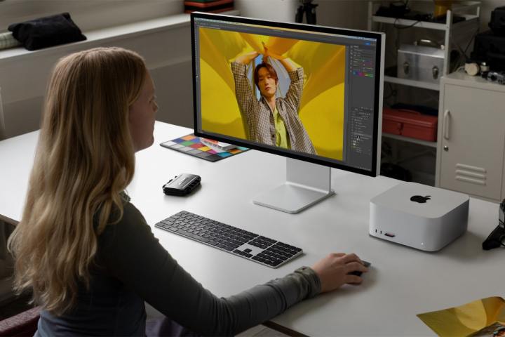 A person uses an Apple Mac Studio and a Studio Display monitor at a desk.
