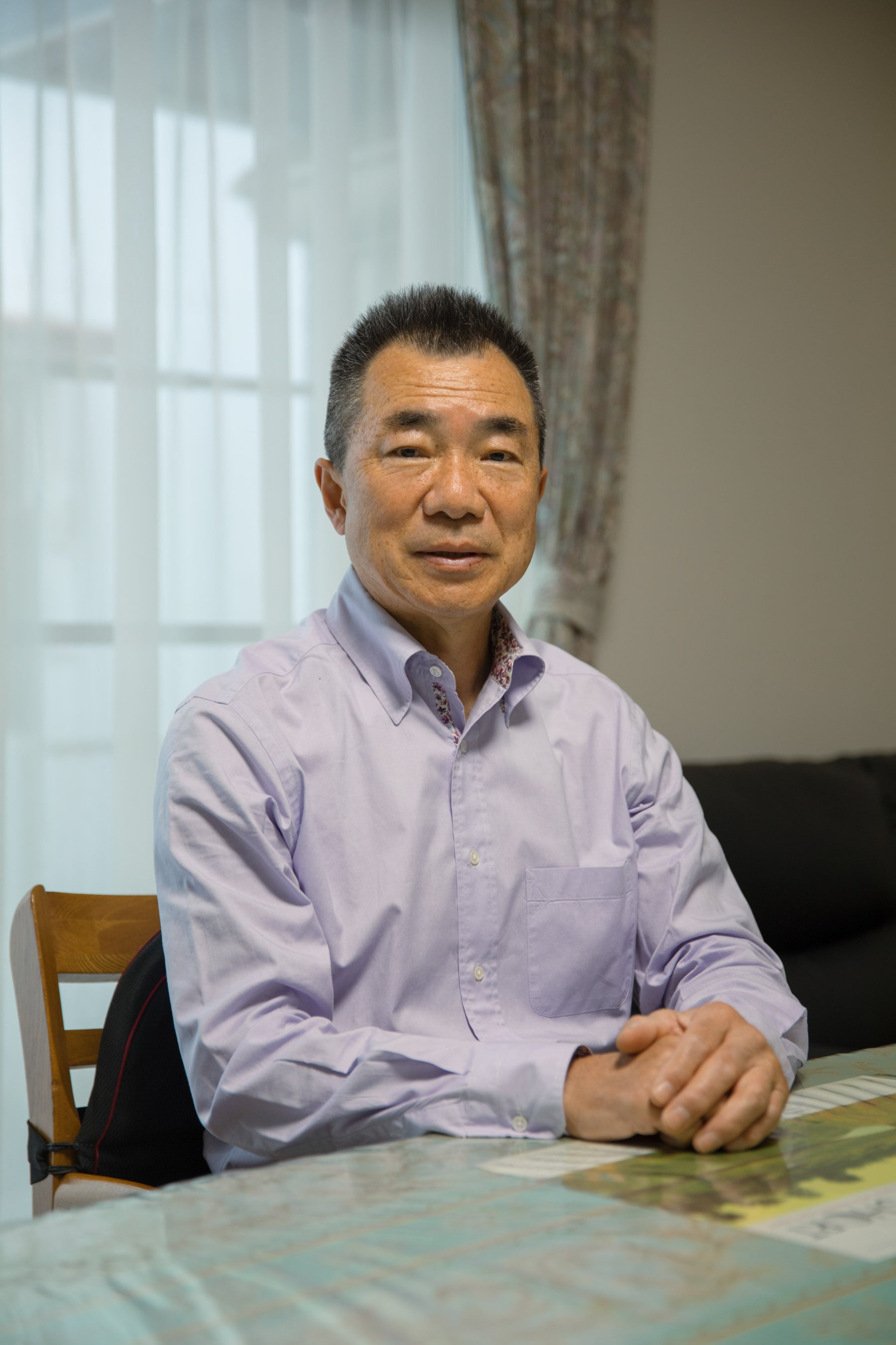 A photo of Mitsuyoshi Hirai, the former chief engineer of the Ocean Link. He sits at a table, his hands folded on a chart.