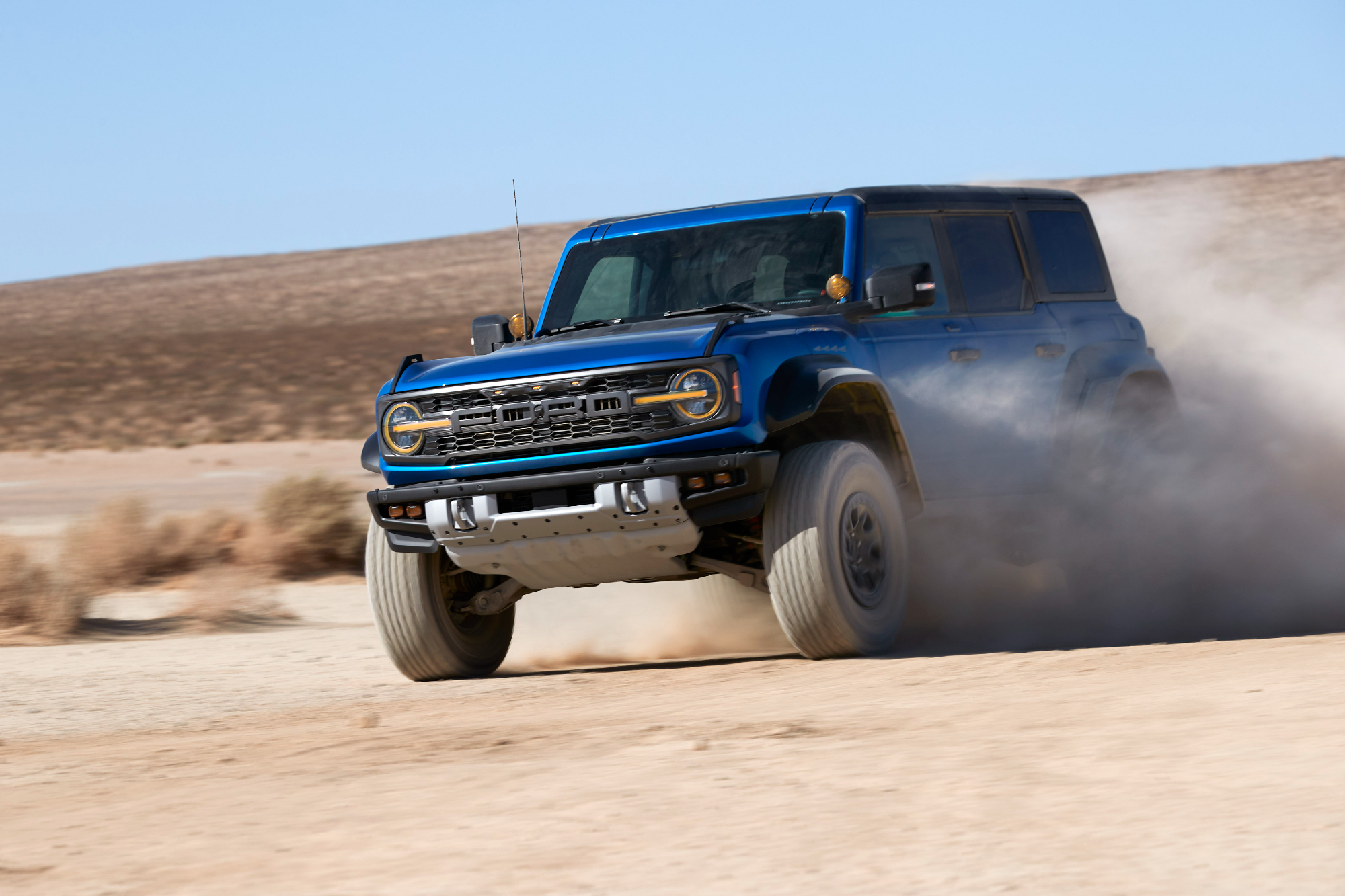 2022 Ford Bronco Raptor off-roadVelocity Blue drifting on desert sand.