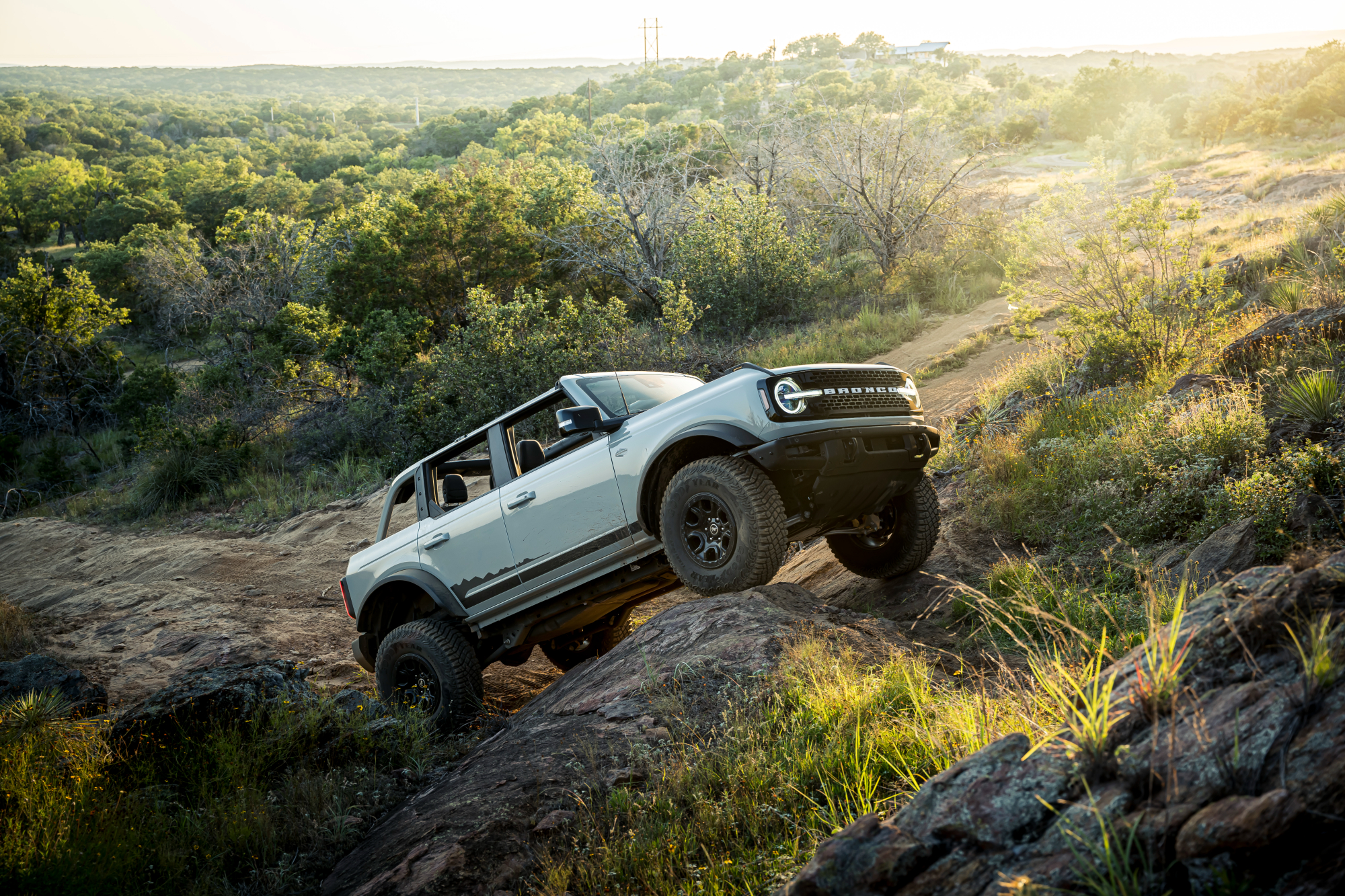 2021 Ford Bronco white body with roof open crawling over large rocks in the outback.