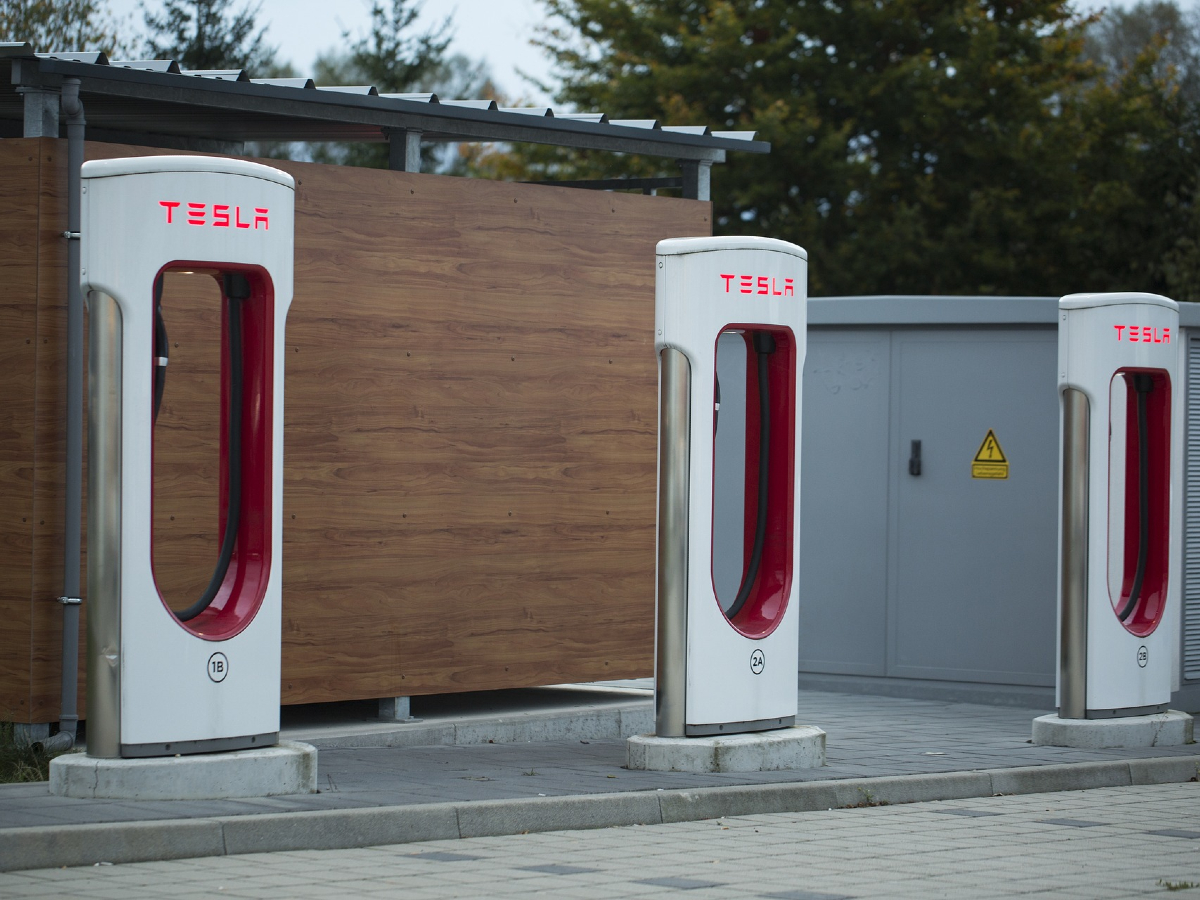 Three Tesla Superchargers beside a low-roofed building.
