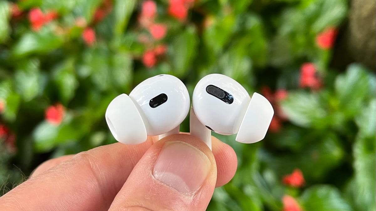 A pair of AirPods with green foliage in the background