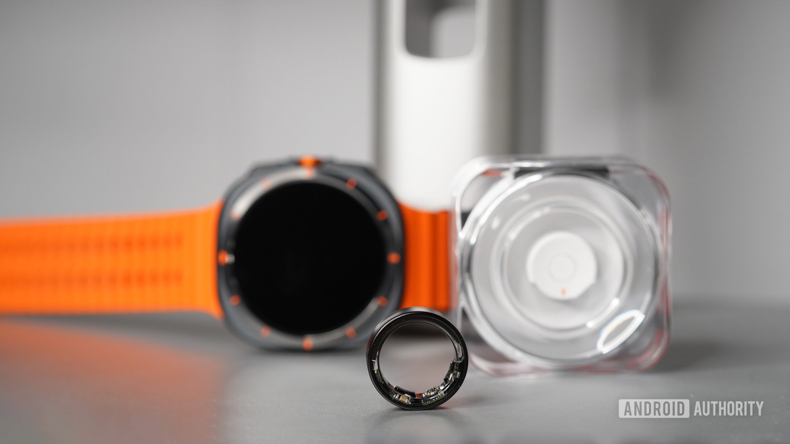 A Samsung Galaxy Ring rests alongside its charging case and a Samsung Galaxy Watch Ultra.