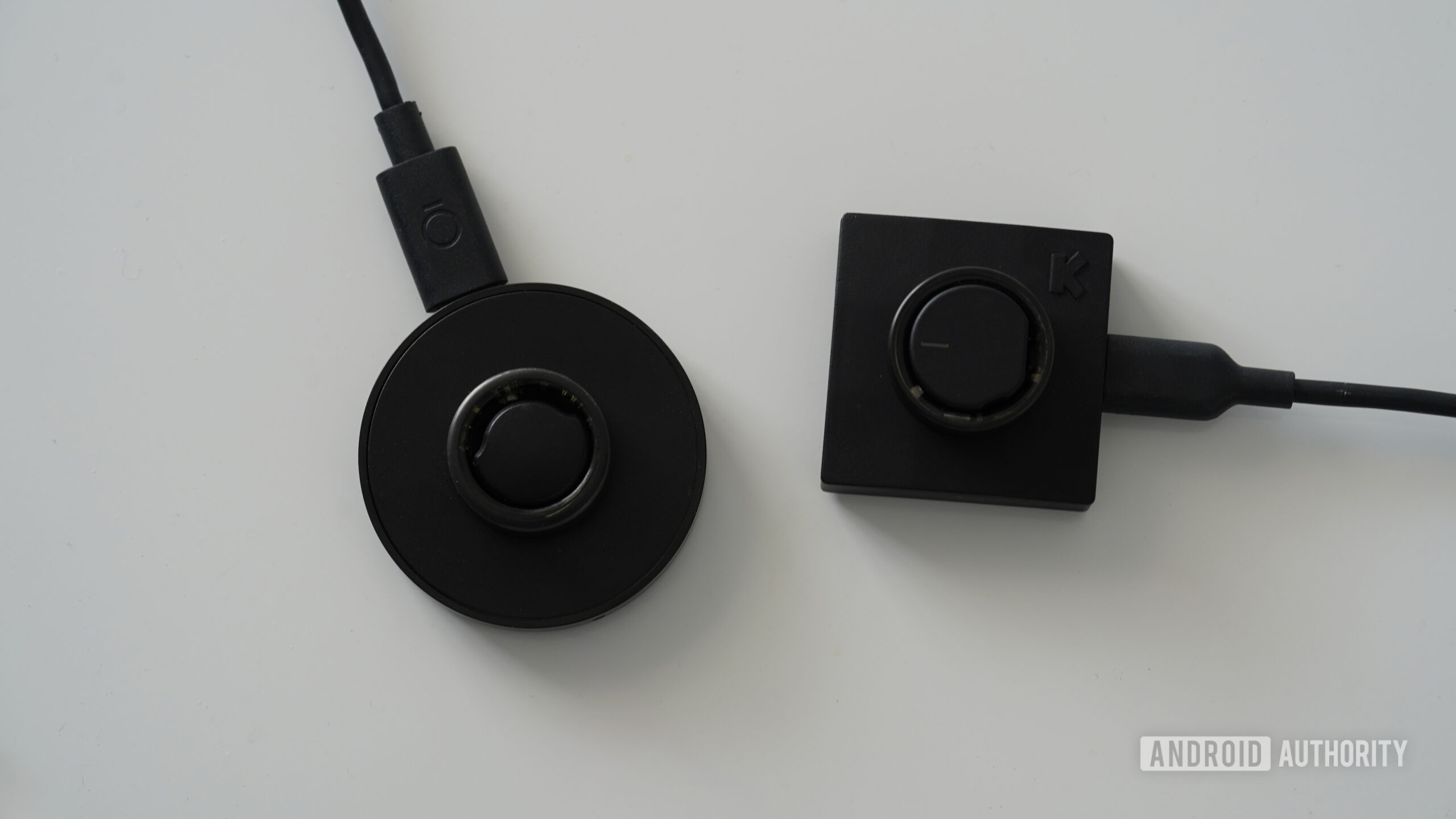 A Ultrahuman Ring Air rests on its charger alongside an Oura Ring 3 also on its charger.