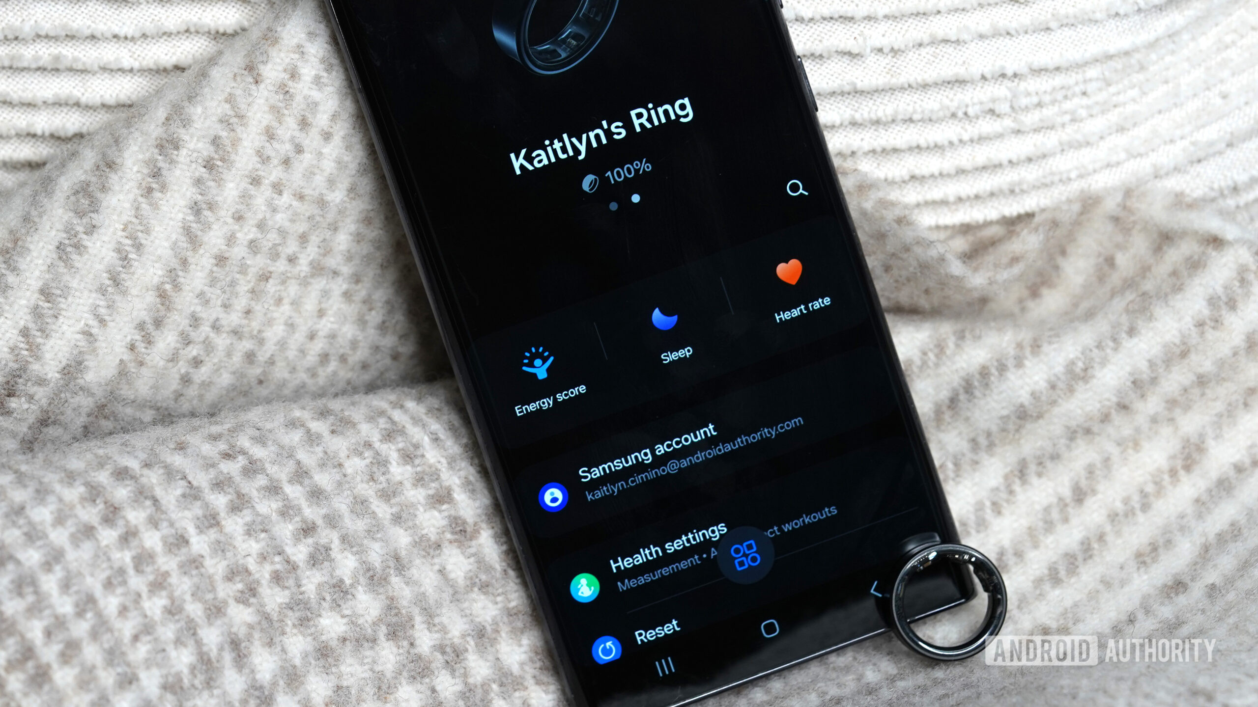 A Samsung Galaxy Ring rests against a Galaxy phone open to the ring's companion app.