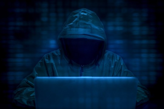 Computer hacker concept image, showing a dark hooded person in a dark room on a laptop