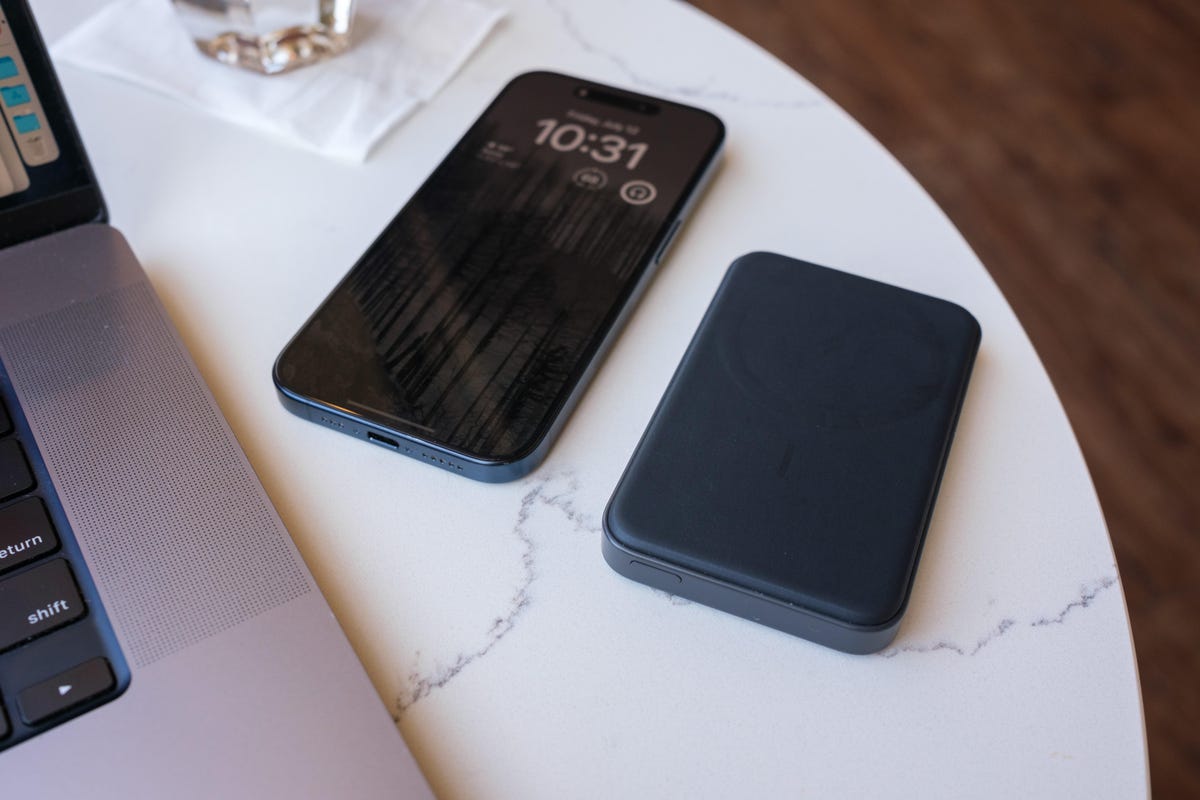 iPhone and a slim portable charger sitting flat on a table in a brightly-lit cafe.