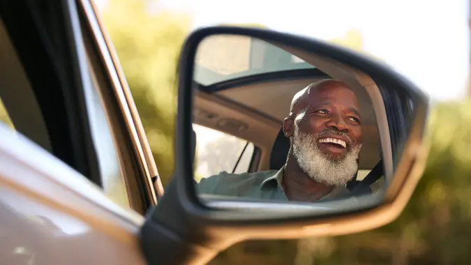 Smiling Senior Male Driver Reflected In Wing Mirror Of Car Enjoying Day Trip Out Driving stock photo