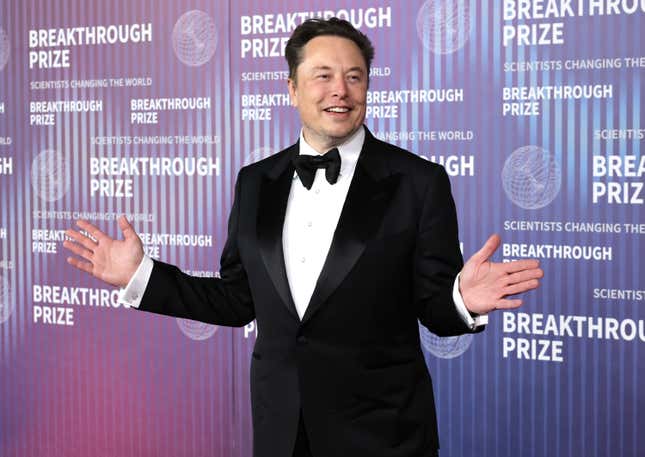 Elon Musk with his arms up in front of a backdrop that says Breakthrough Prize