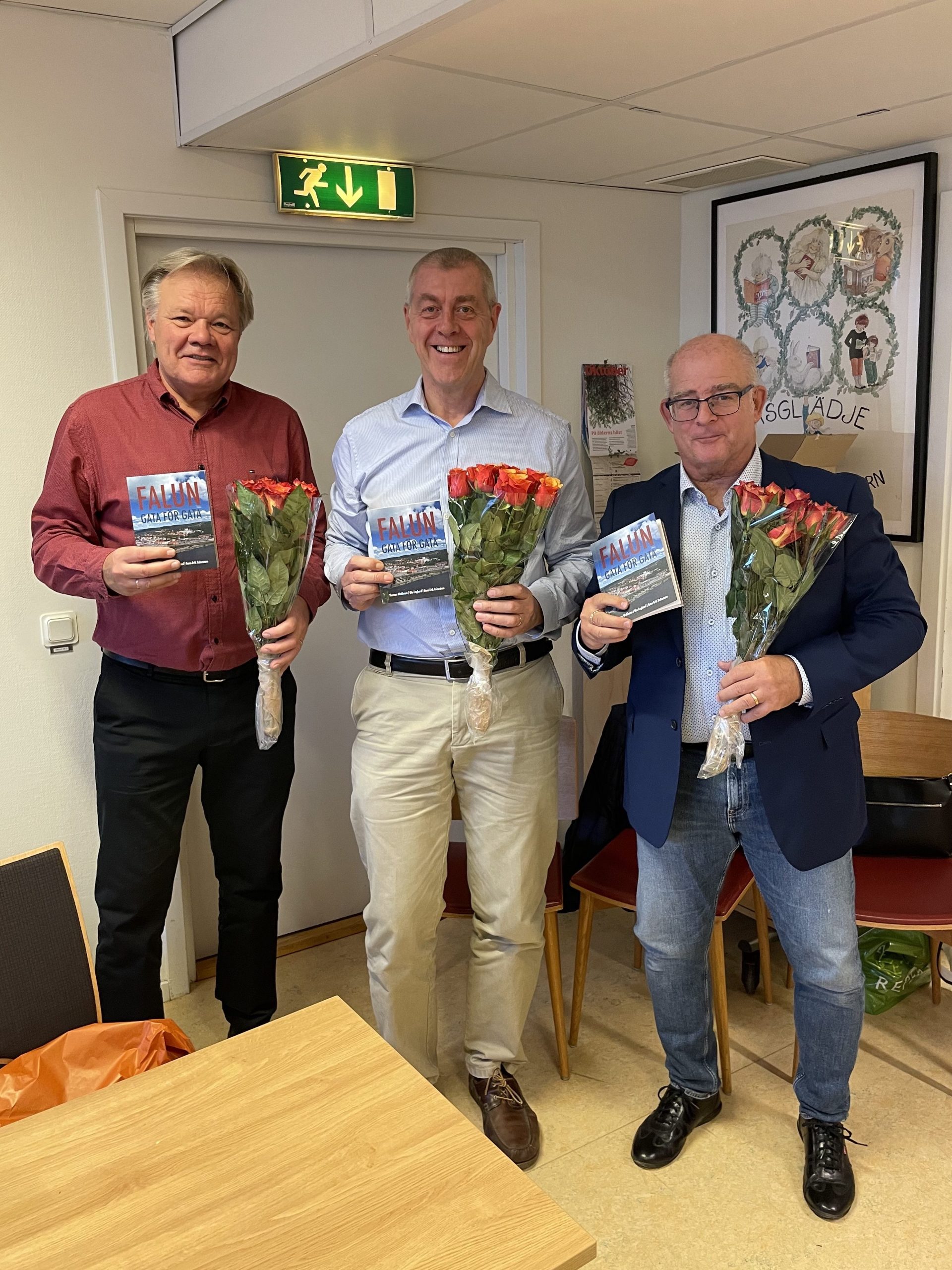 Tre glada herrar med boken Falun Gata för Gata och varsin blombukett.