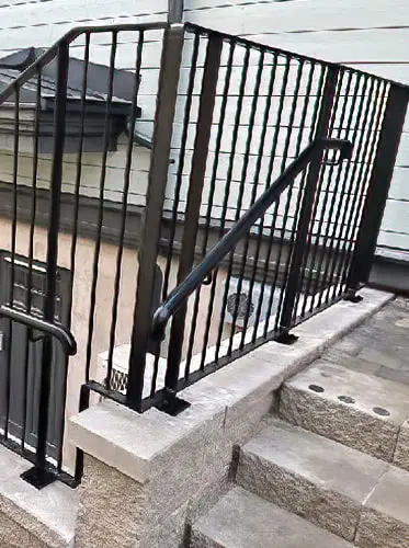 Ett svart smidesräcke och staket monterat på en stentrapp