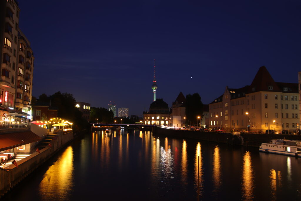 Foto zur blauen Stunde mit Blick über die Spree in Berlin Richtung Bode-Museum. Im Hintergrund ist er Fernsehturm am Alexanderplatz zu erkennen.
Die Lichter der Restaurants und Museen spiegeln sich in der dunklen Spree.