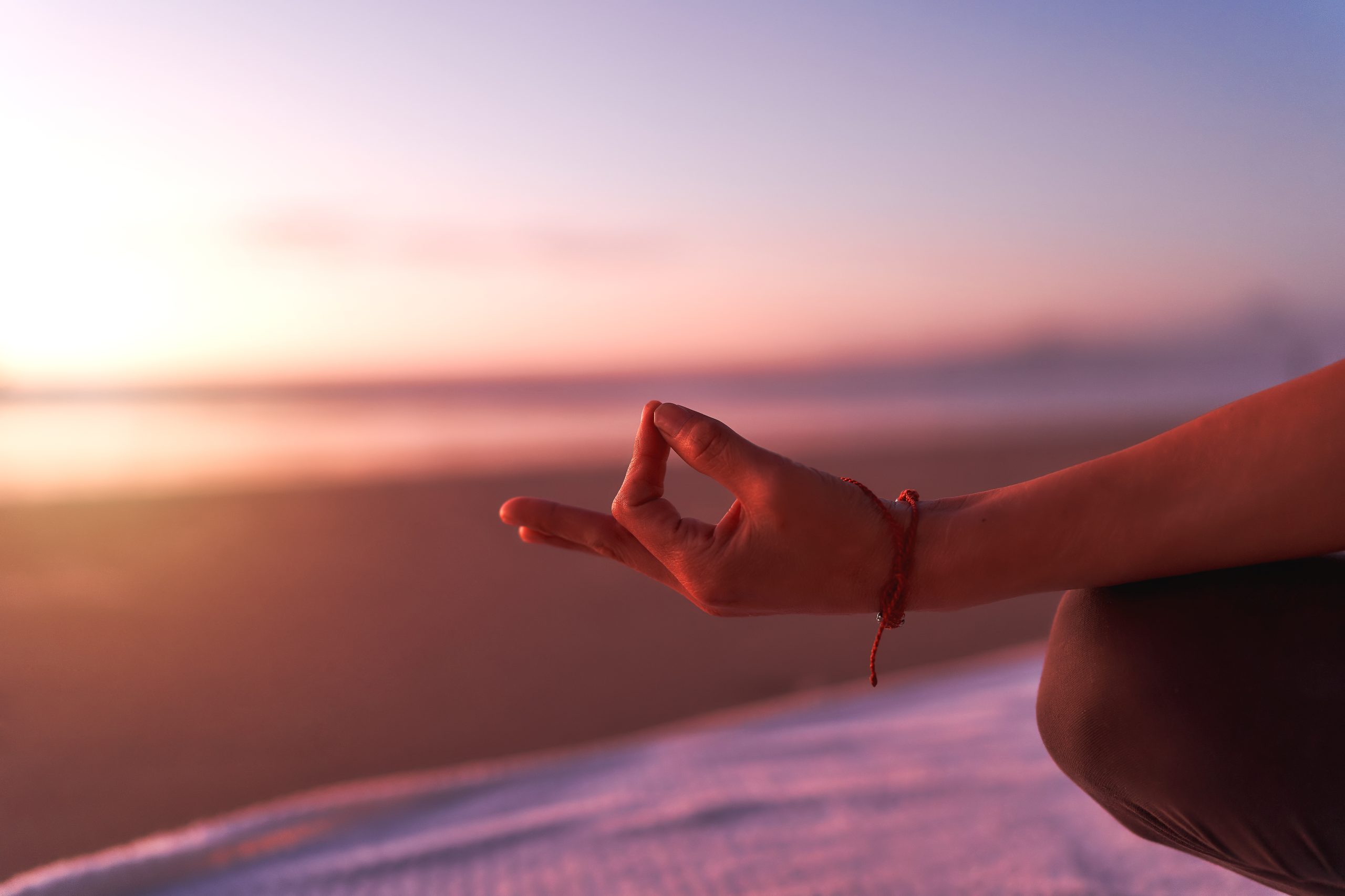 view of hand in meditation or yoga mudra on the beach at sunset