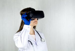 Person in a lab coat with a stethoscope around their neck looking through a Virtual Reality head set. 