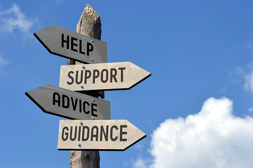 Wooden singpost with "help, support, advice, guidance" arrows against blue sky.