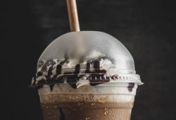 A vertical closeup of a plastic cup of cold coffee with a vanilla cream.